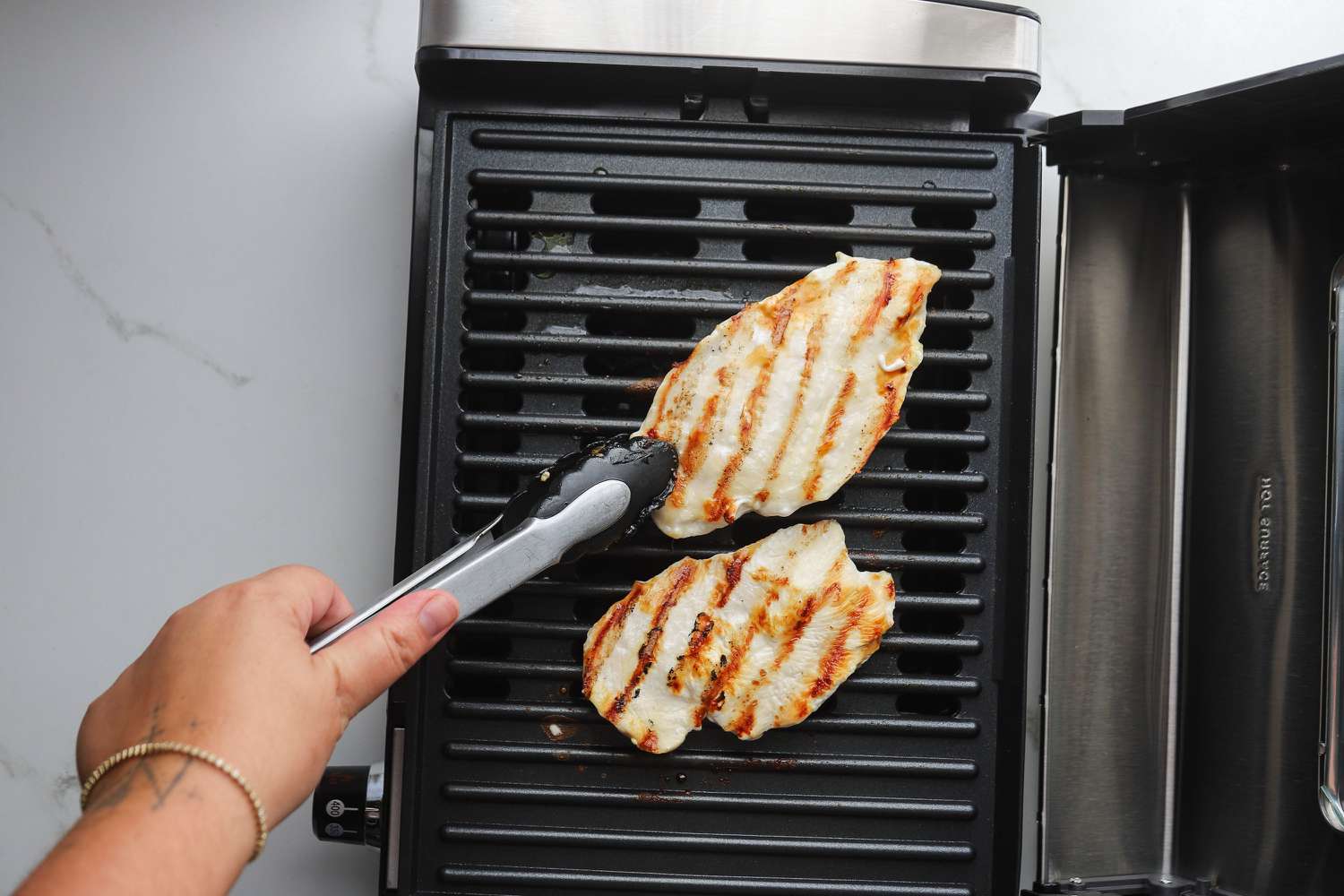 A person flipping grilled chicken on the Hamilton Beach indoor grill