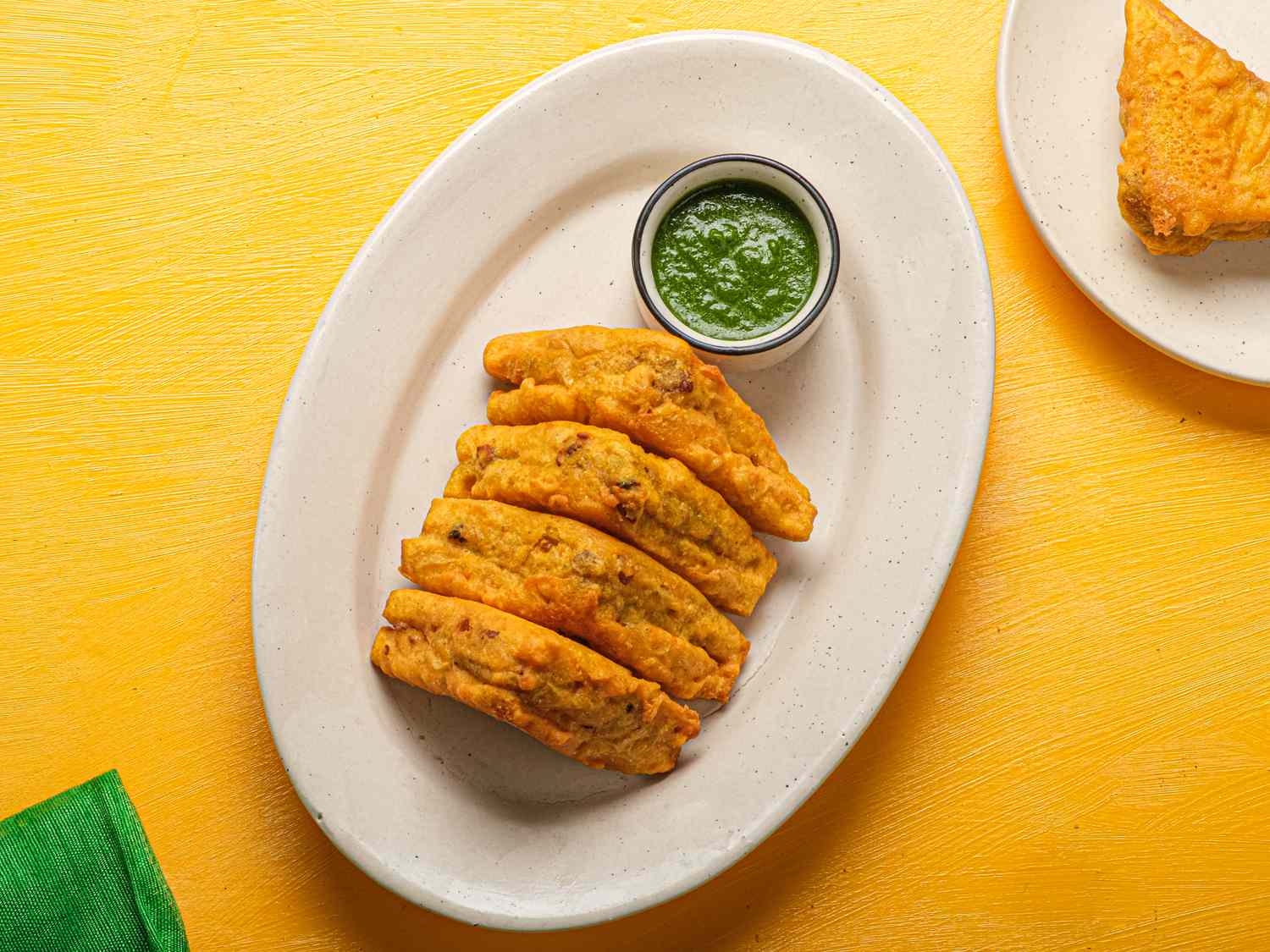 Overhead view of bread pakora on an oval platter with a green dipping sauce.