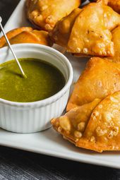 Samosas on a serving plate with a ramekin of herb chutney alongside