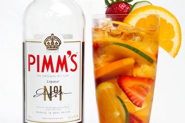 A bottle of Pimm's liqueur next to a fully garnished tall glass of Pimm's Cup cocktail.