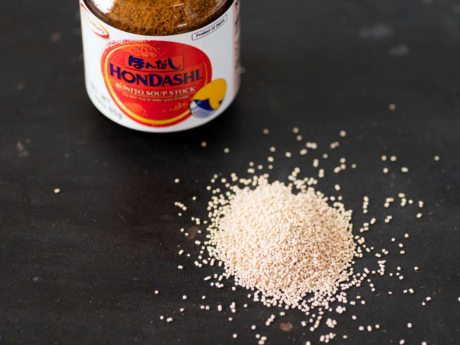 A jar of hondashi next to a small loose pile of instant dashi granules.