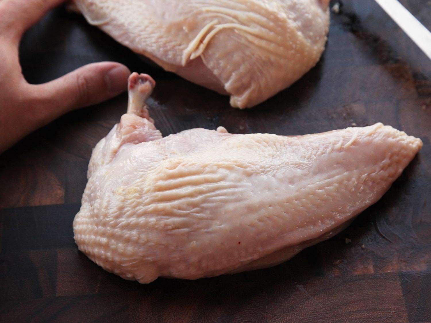 An airline-cut chicken breast resting on a cutting board.