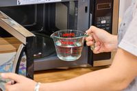 A hand putting a cup of water into the Farberware Countertop Compact Microwave (FMWO11AHTBKB) 