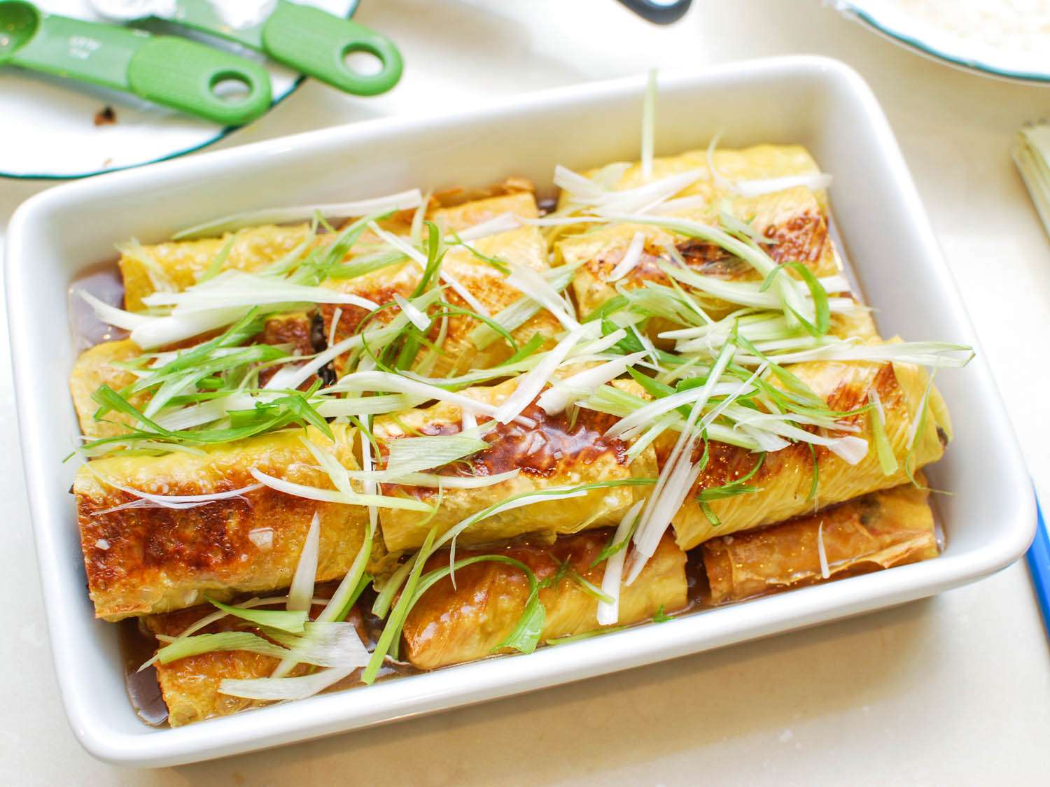 A baking dish filled with bean curd rolls, thickened chicken stock, and sliced scallion.