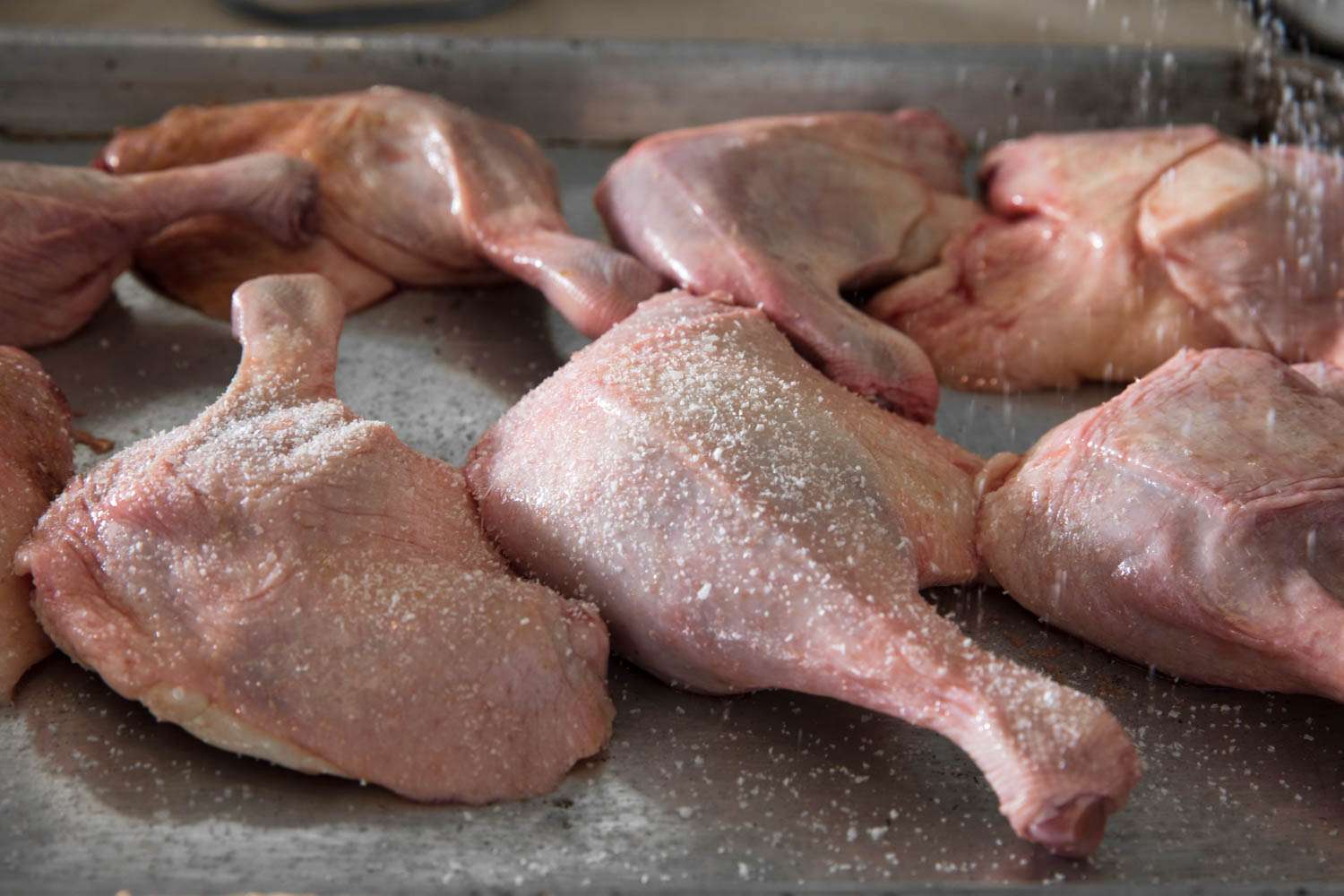 Salting raw duck legs on a baking sheet.