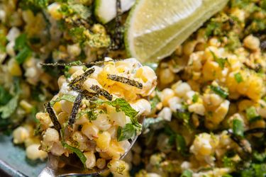 A dish of corn salad with herbs lime wedge garnish and nori strips visible