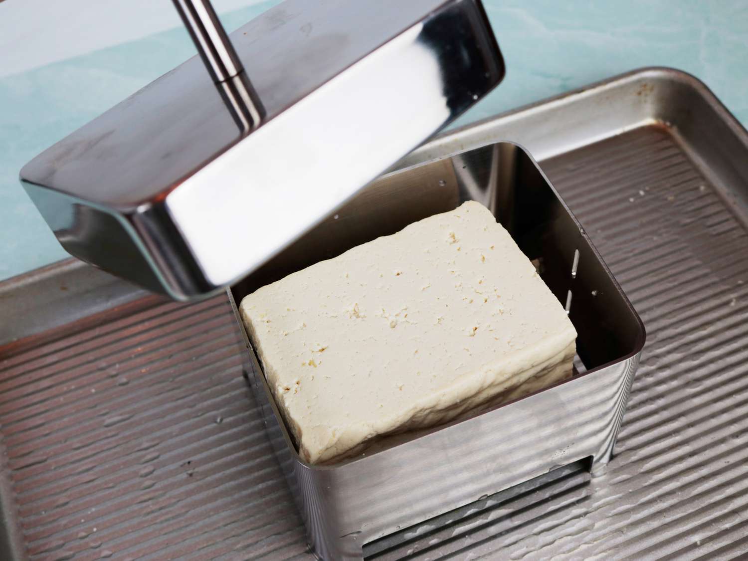 a tofu press resting on a sheet pan to catch the water