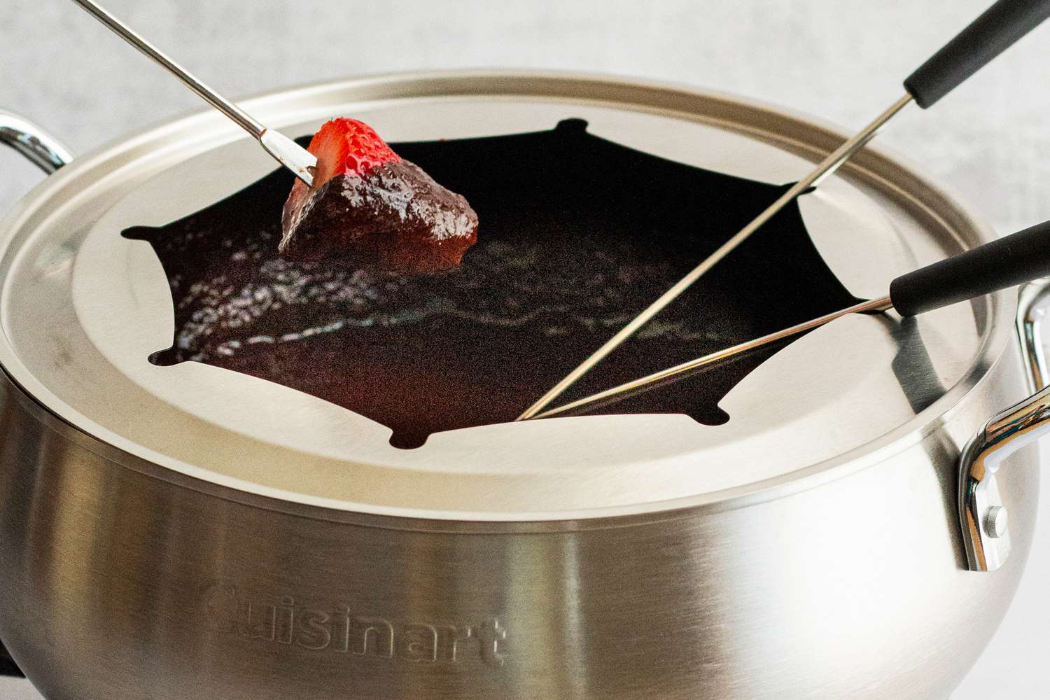 A strawberry being dipped into chocolate fondue in the Cuisinart fondue pot.