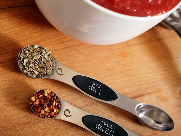 Measuring spoons full of dried oregano and red pepper flakes.