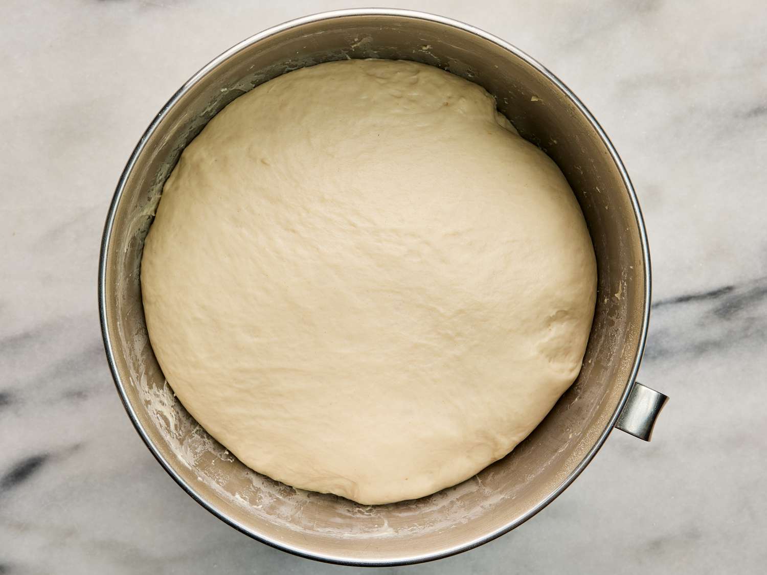 Dough in bowl after proving. Metal bowl on white marble surface 