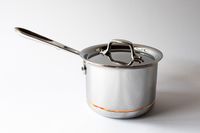 A stainless steel saucepan with a lid and a long handle against a plain background