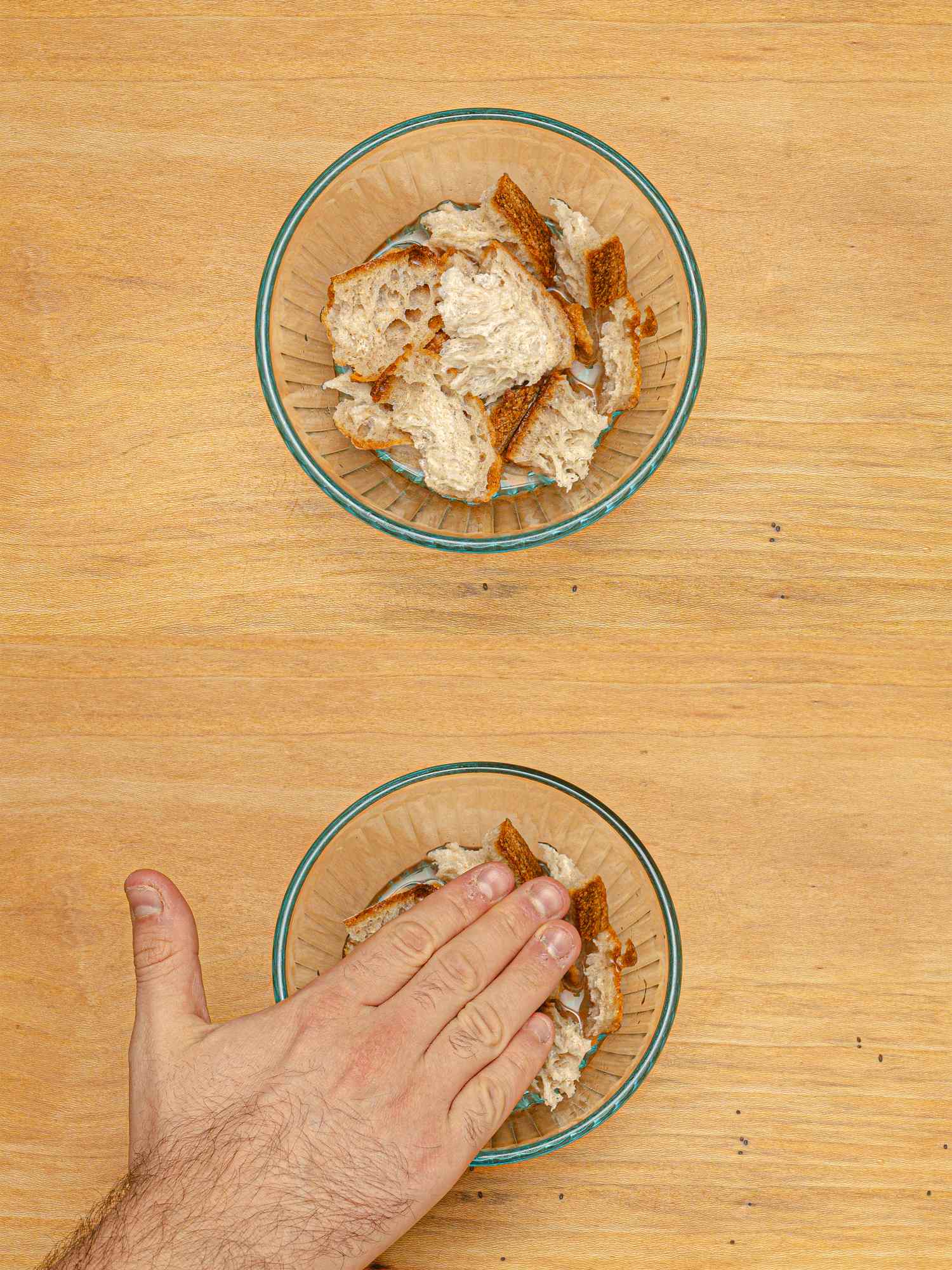 A hand pressing food in a bowl with another bowl of food above it on a wooden surface