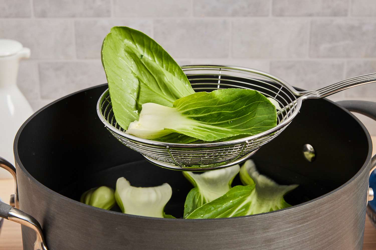 A metal spider strainer lifting bok chou from a stockpot