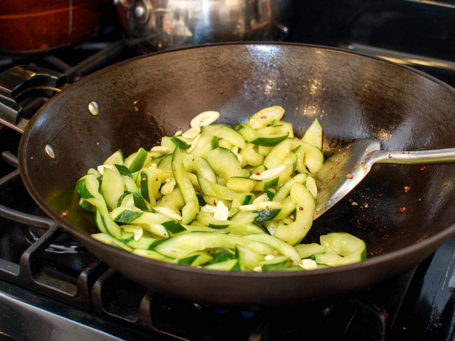 Cucumbers, garlic, and chile flakes being stir-fried in a wok.