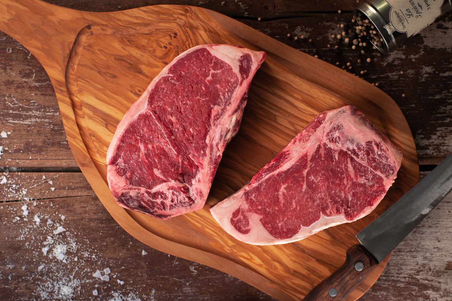 Two raw steaks on a wooden cutting board with a knife beside them