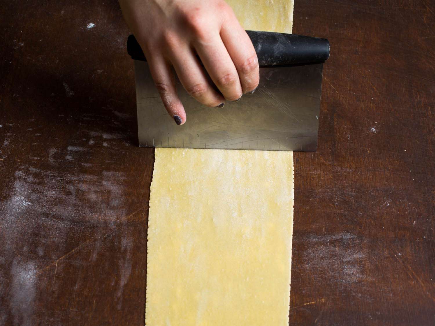 Dividing a sheet of pasta dough in half with a bench scraper.