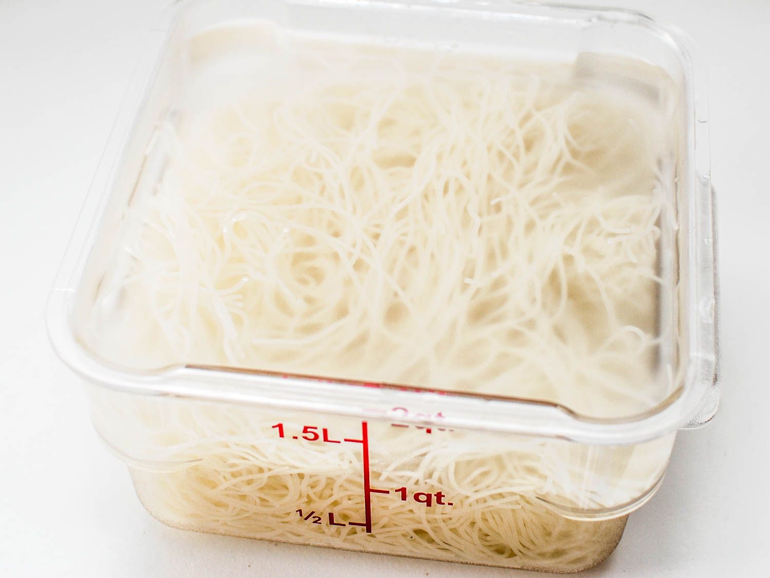 Rice vermicelli noodles sitting in a clear Cambro container with boiling water.
