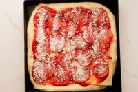 A pizza ready prepared for the oven in the LloydPans 12x12x1.5 inch Sicilian Style Pizza Pan