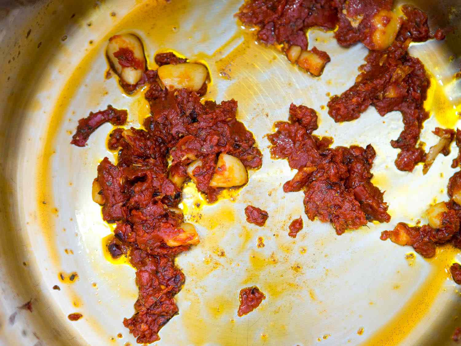 Sautéed tomato paste in pot with garlic, aromatics, and olive oil for quick Italian-American red sauce.