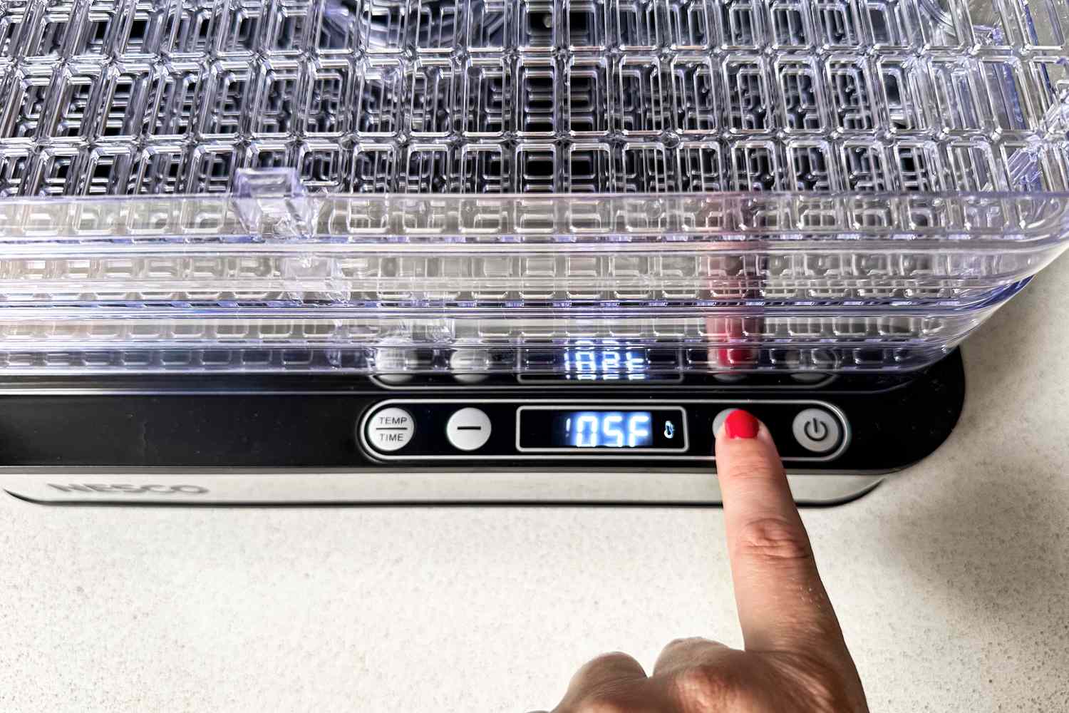 A person pressing the power button on a Nesco Digital 5 Rectangular Dehydrator set to 105 degrees Fahrenheit