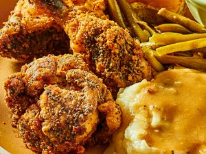 Dish of fried chicken with coleslaw, greenbeans, and mashed potatoes, with a fork and serving dishes in the background