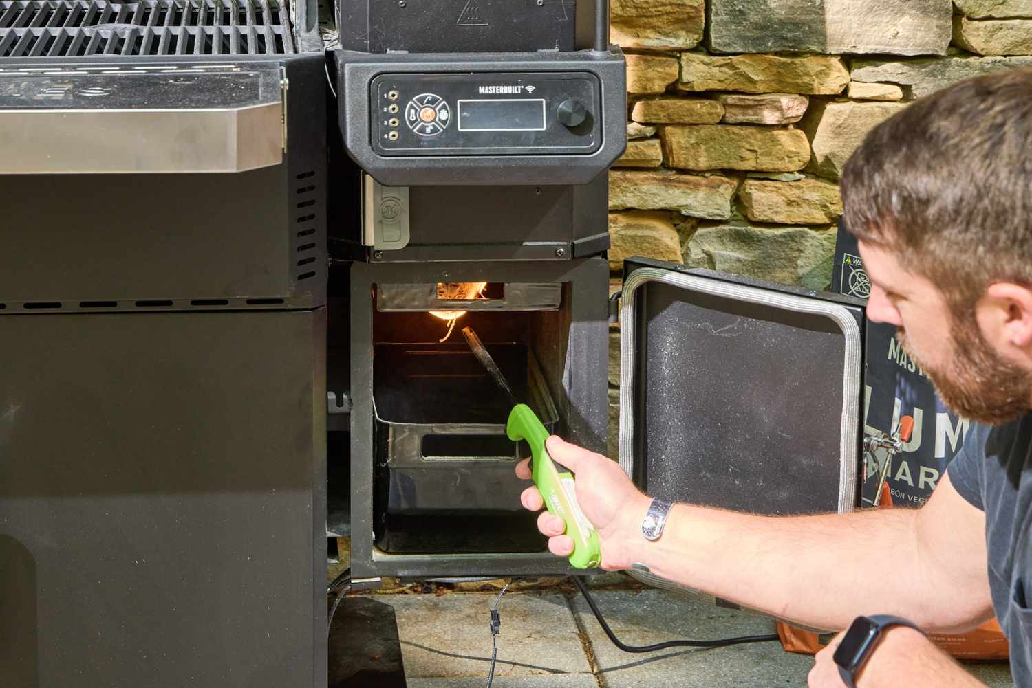 A person lights the pilot light on the Masterbuilt Gravity Series 1150 Digital Charcoal Grill and Smoker