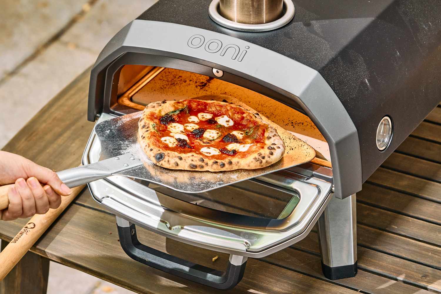 A person removes a pizza cooked in the Ooni Karu 2 Multi-Fuel Pizza Oven