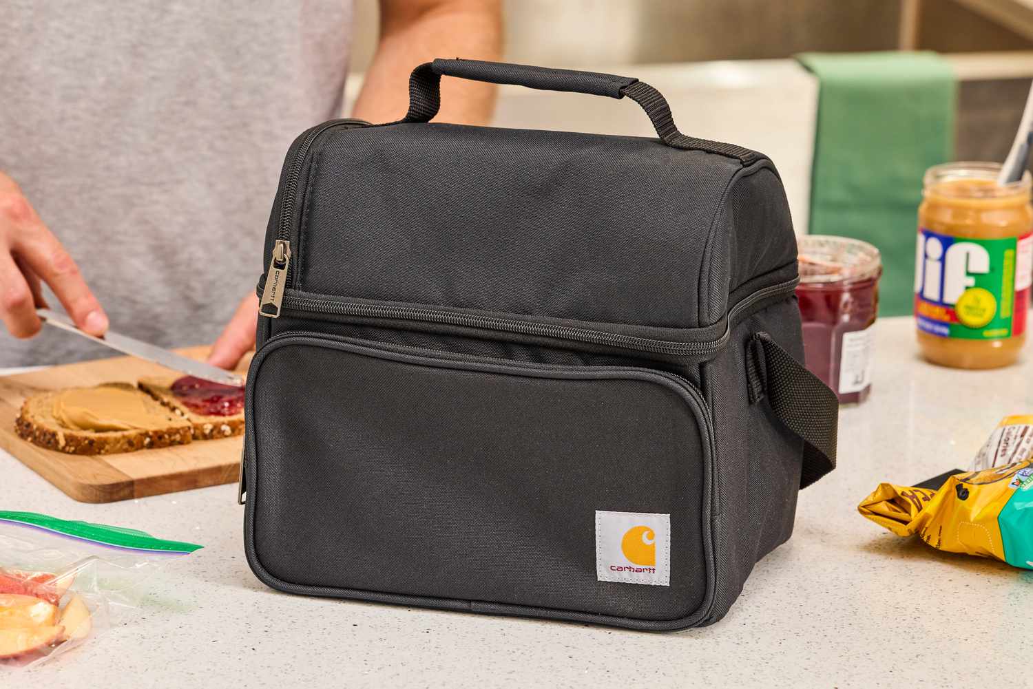 Black Carhartt lunch box on a countertop in front of a person making a sandwich