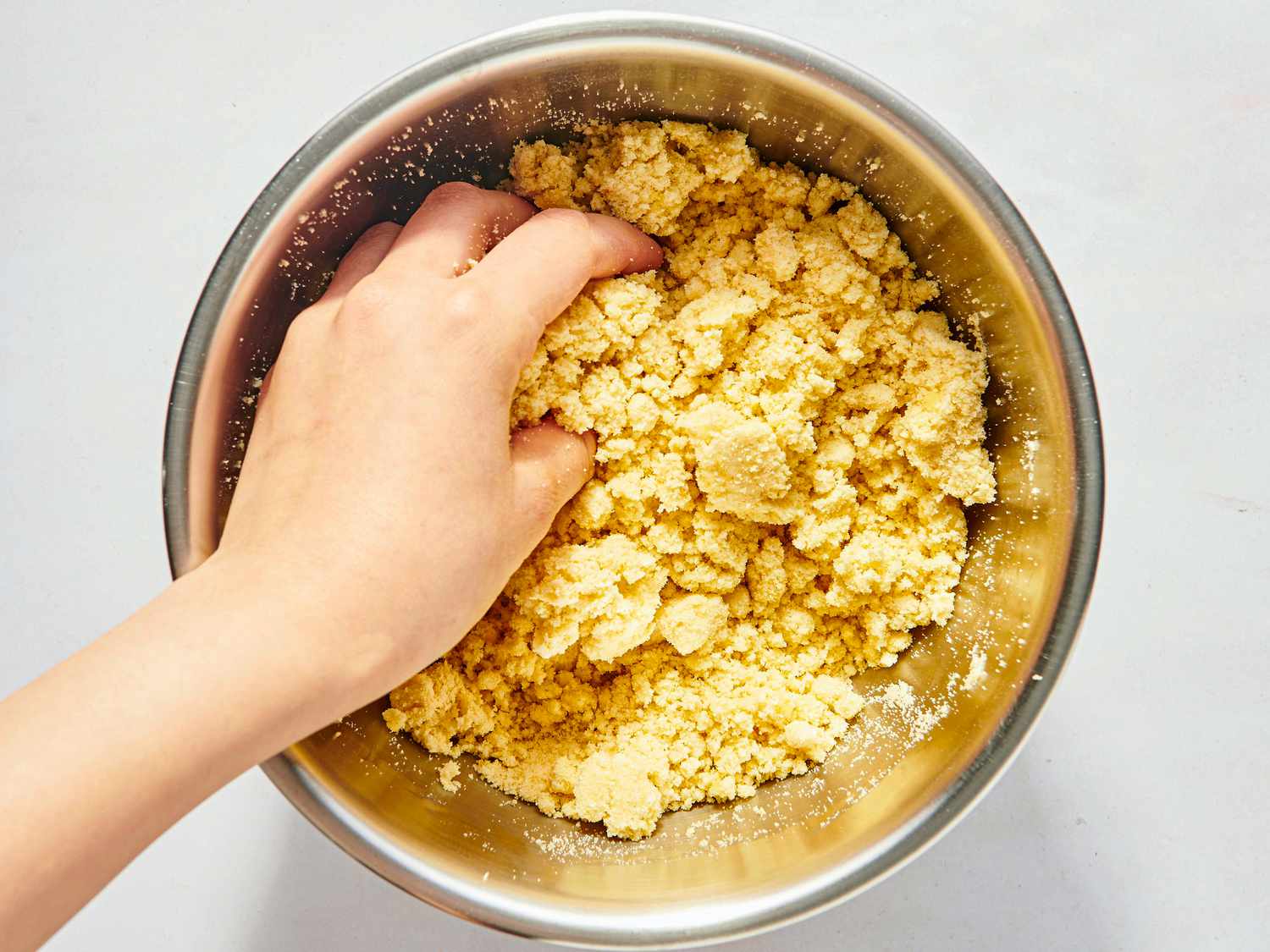 hands pressing dough together in metal bowl