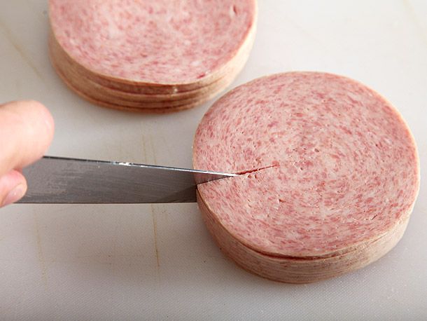 Slices of pork roll being scored in stacks.