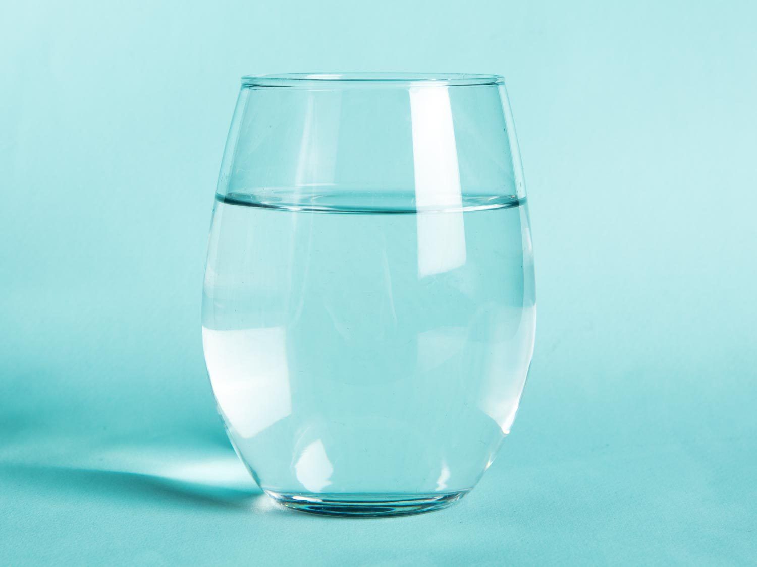 A glass of water against an aqua background.