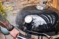 A person opens the Weber 18201001 Summit Kamado E6 Charcoal Grill