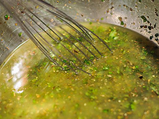 Whisking together marinade ingredients, including olive oil, lemon juice, and fresh herbs, for chicken spiedie recipe.