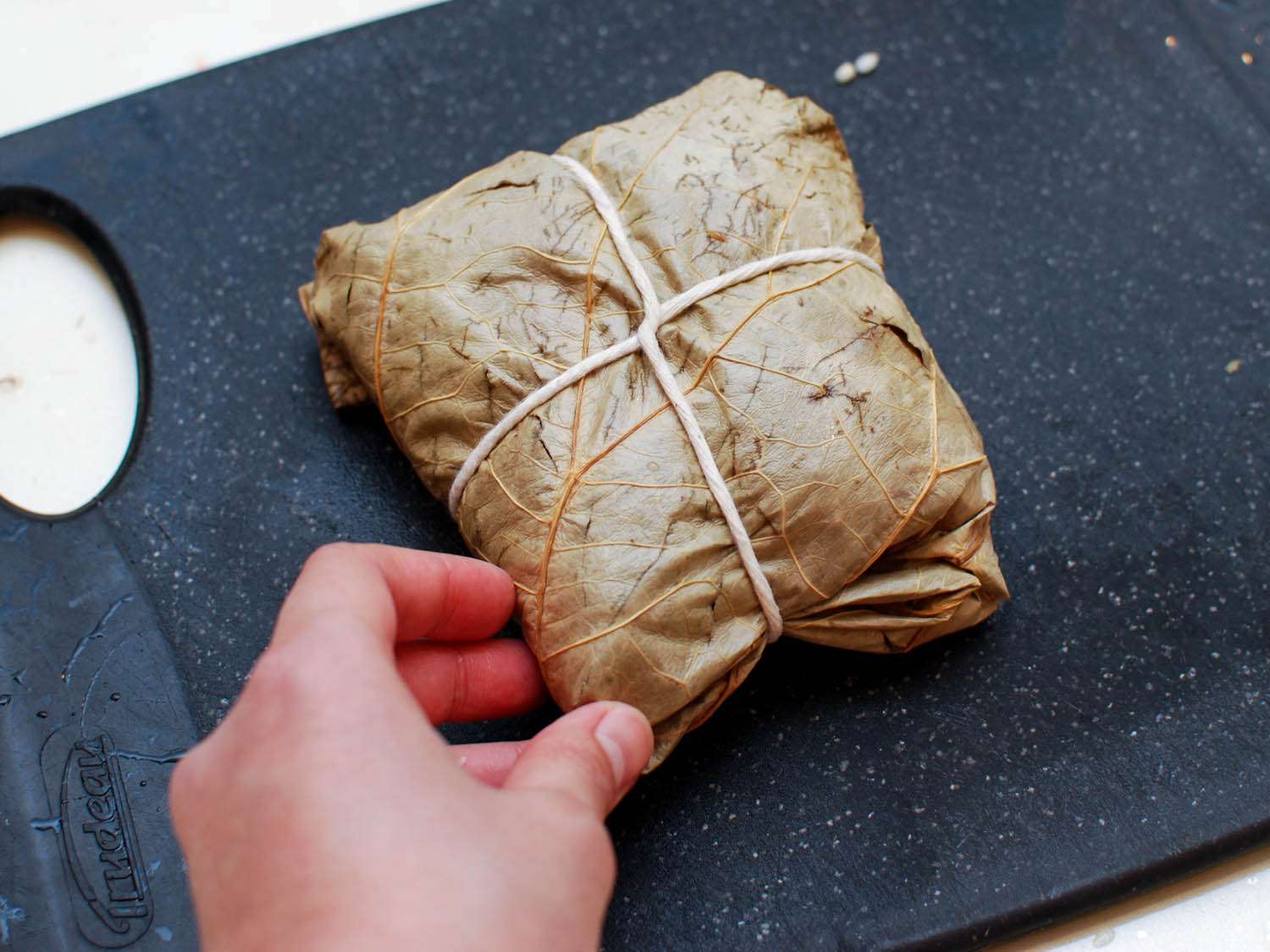 A sticky rice package tied up with twine on a black cutting board.