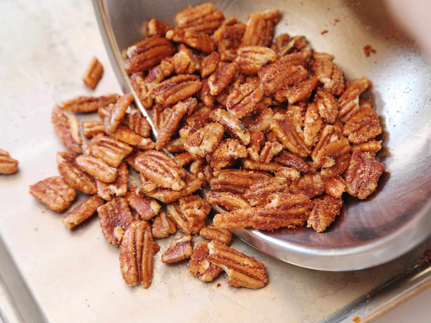Transferring pecans that have been tossed in a spice mix to toast in a baking sheet. 