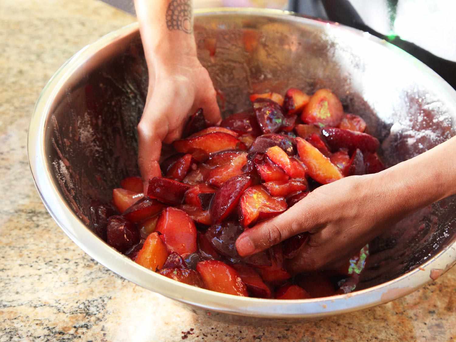 Plums are tossed with sugar in a large bowl and left to macerate.