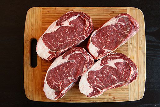 Four fresh steaks on a cutting board, ready to be dry-aged at home.