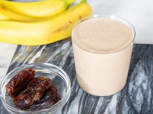 A bananadate smoothie in a glass bananas and dates beside it