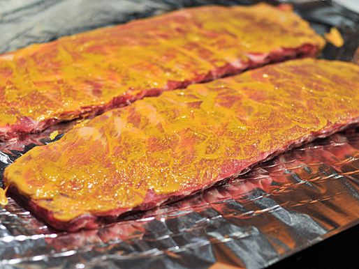 Two St. Louis-style rib racks brushed with mustard sitting on foil.