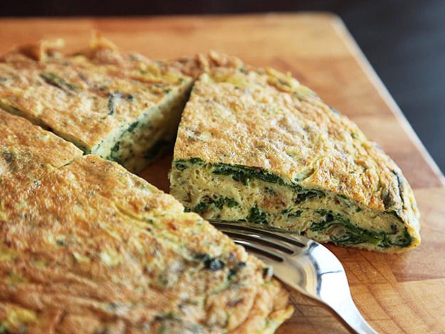 A puffy ramp frittata with a wedge cut out so we can see the inside. There's a fork on the cutting board next to the frittata wedge.