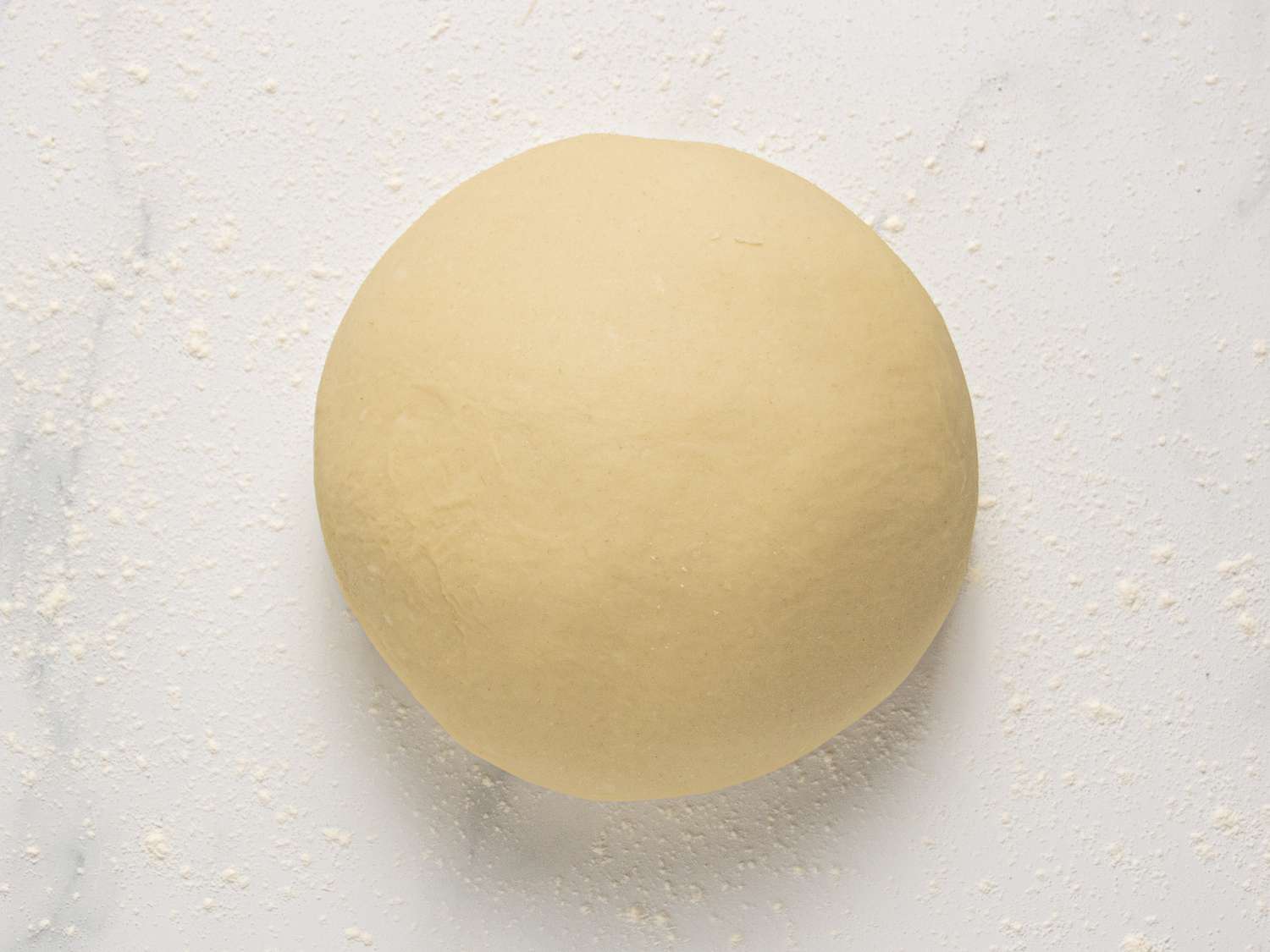 Dough kneaded into a large ball on a floured surface 