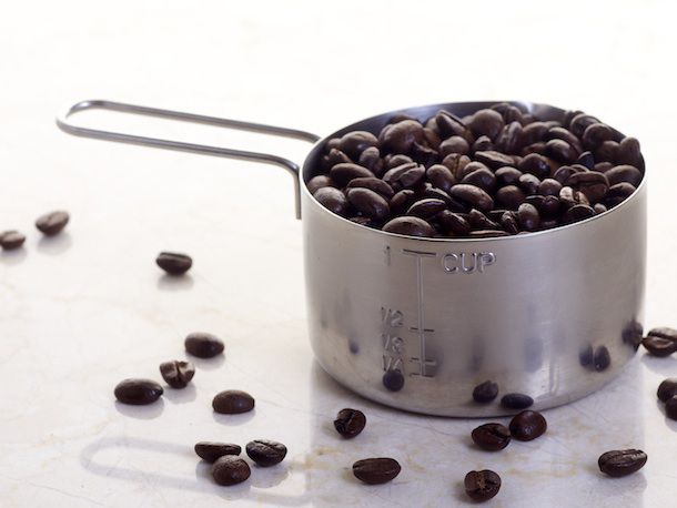 A 1-cup measuring cup filled with whole coffee beans.
