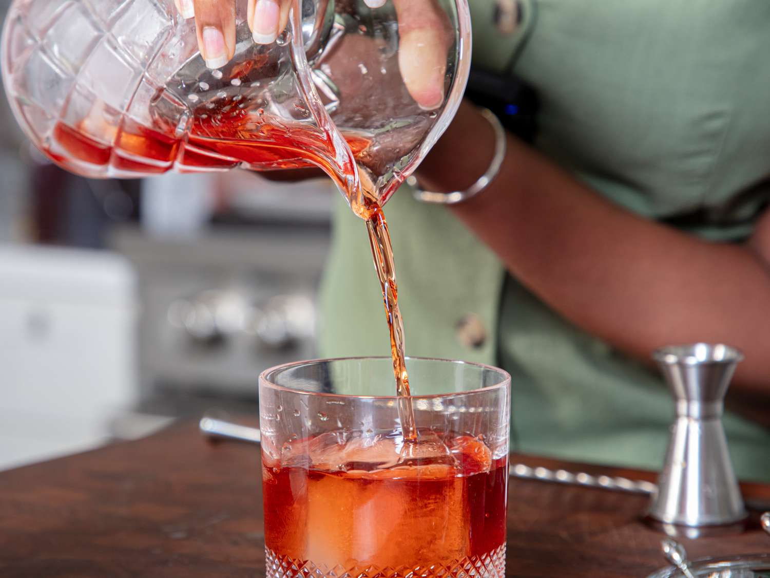 Person pouring a drink into a glass using a mixing glass