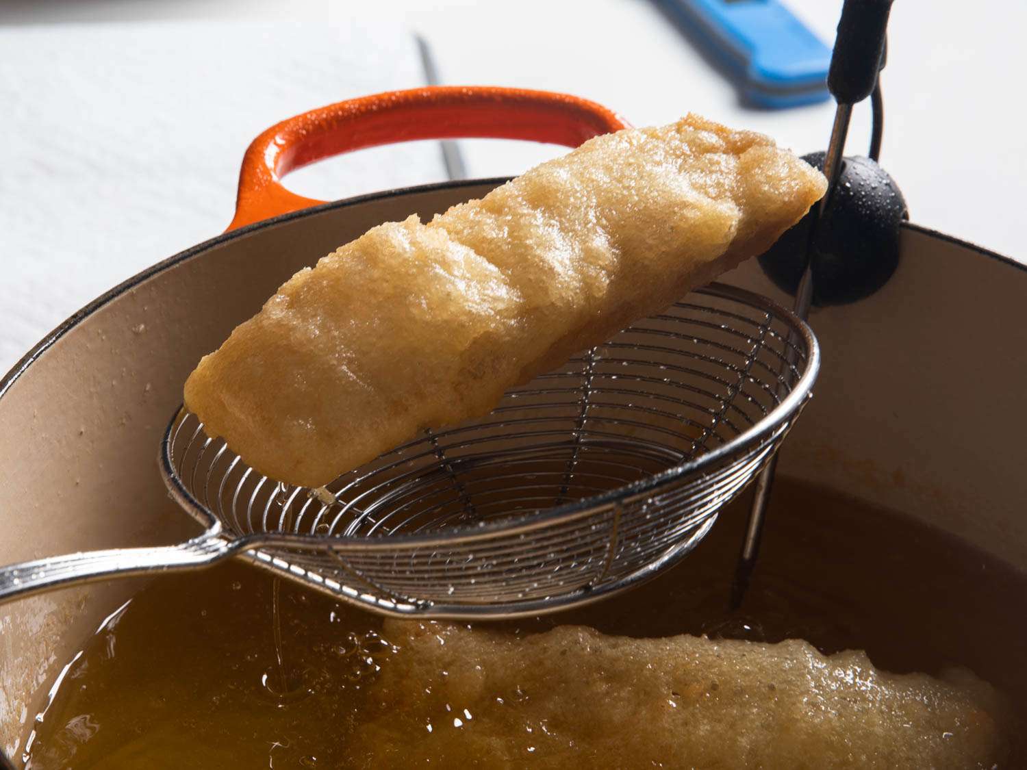 Lifting a fried fillet out of a pot of oil with a spider skimmer
