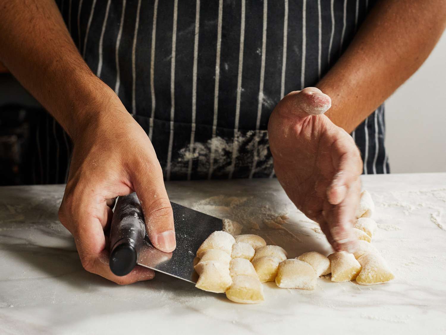 A person uses a bench scraper to lift up a pile of gnocchi