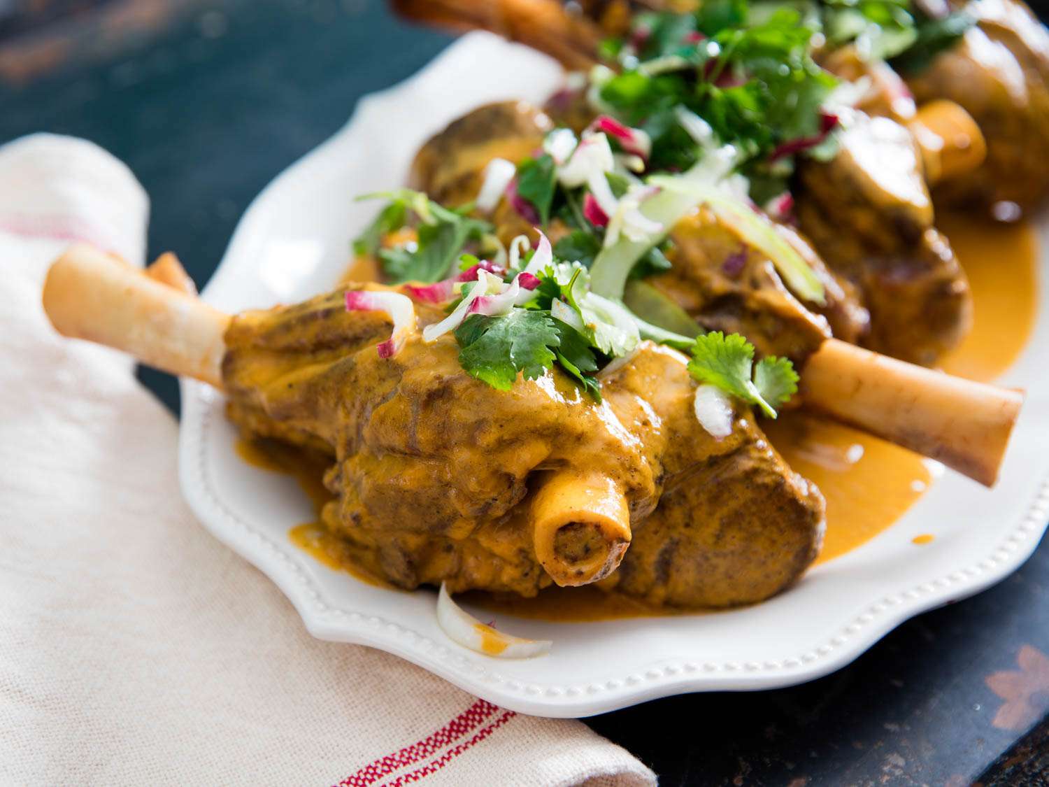 Closeup of Tender Braised Lamb Shanks With Bitter Herb Salad, served on a white platter.