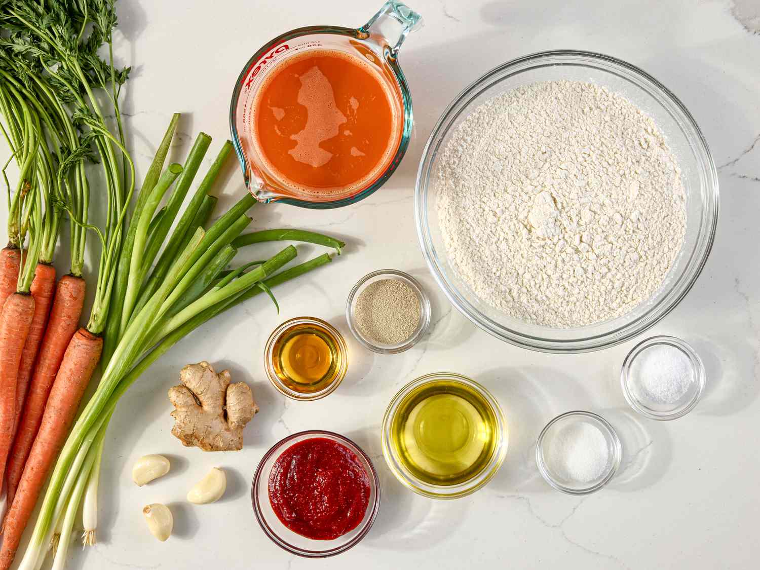 Ingredients arranged for preparing a recipe, including carrots, green onions, flour, ginger, and various liquids in small bowls