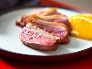 Medium-rare duck breast sliced and served on a plate with orange wedges