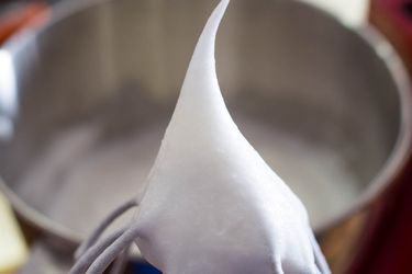 Beaten egg whites standing in a peak on the whisk of a mixer. 