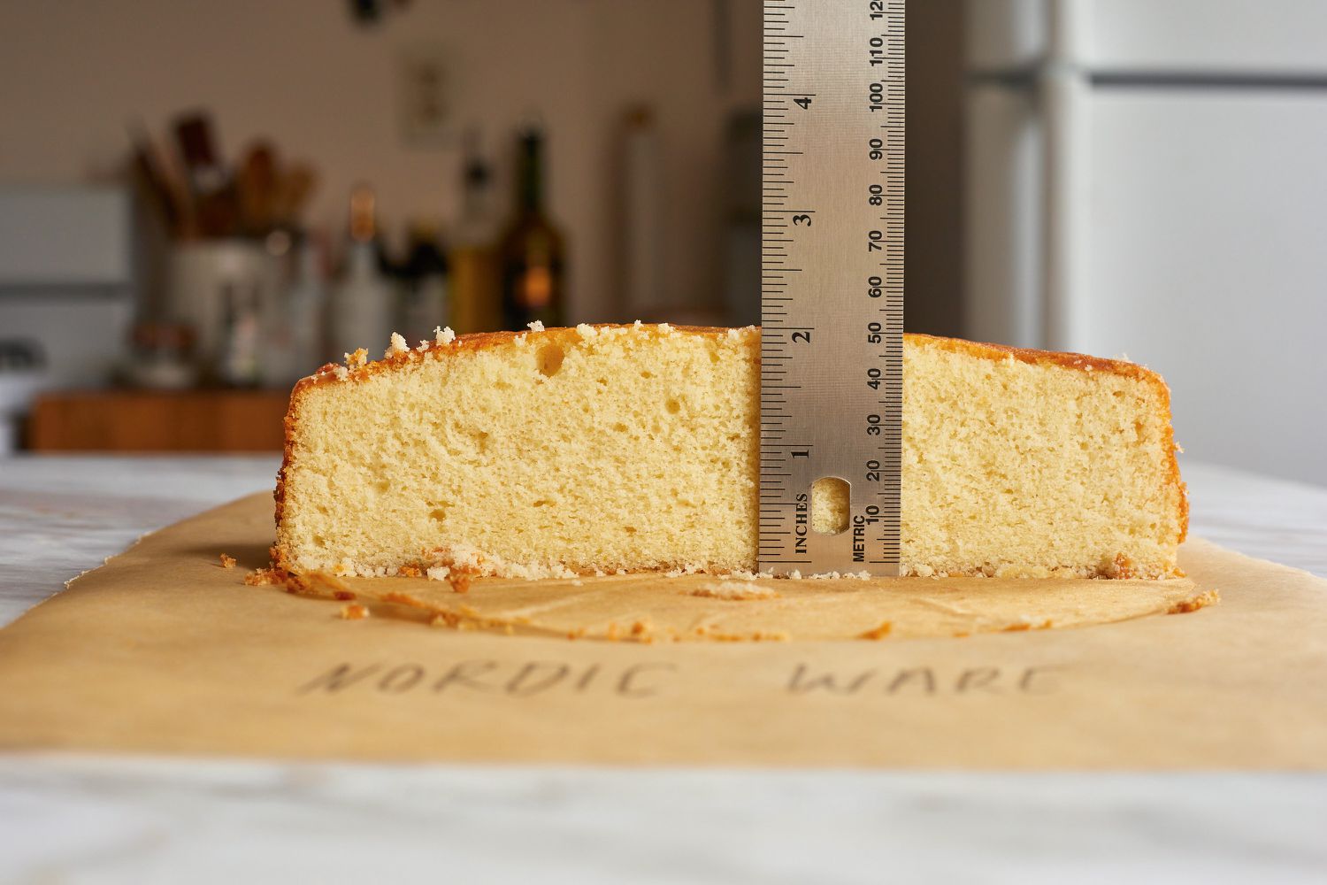 a person using a ruler to measure the rise of a half of a cake layer